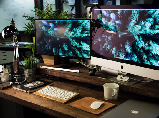 A busy desk with two computer monitors, a notebook and a MacBook