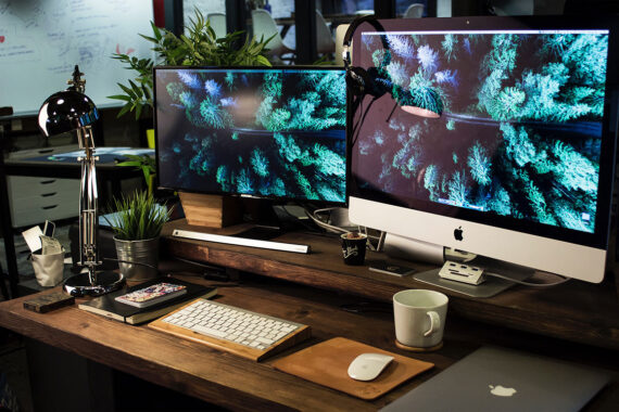 A busy desk with two computer monitors, a notebook and a MacBook