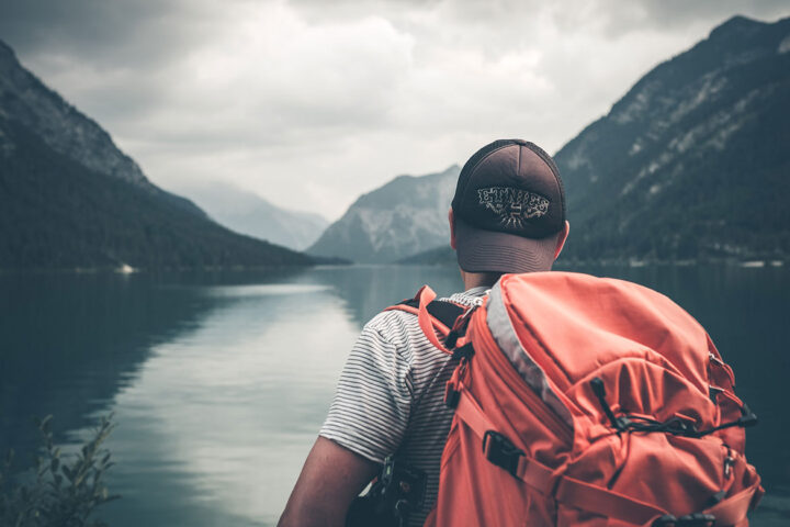 Hiker with a heavy backpack looking out at mountains and still water