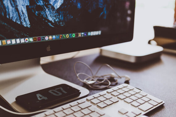 Close-up of a desk with an iMac and a smartphone displaying the time